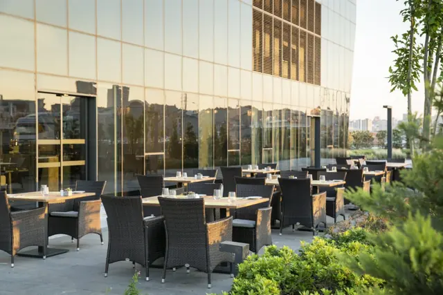 Terrasse avec tables et fauteuils en osier au pied de l’hôtel